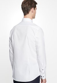 Witte overhemd met lange mouwen, een spitse kraag, knoopsluitingen aan de manchetten en een gladde stof. De achterkant toont een slim fit en nette stiksels.