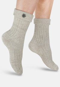 Stricksocken in hellbeige mit gerippter Textur und umgeschlagenen Bündchen. Mit einem dekorativen Metallblumenakzent am Bündchen.
