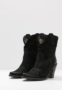 Botas de vaquero de ante negro hasta el tobillo con punta afilada, tacón bajo y apilado, y un forro interior a rayas colorido. Costura detallada en la parte delantera.