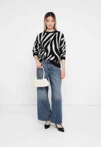 Sort-hvidstribet sweater, blå brede jeans, sorte spidse sko og en lille hvid taske. Glat stof og afslappet pasform.
