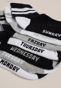 Set med veckodagsstrumpor i svart, vitt och grått. Varje strumpa visar en veckodag i fet stil. Randiga muddar på vissa par.