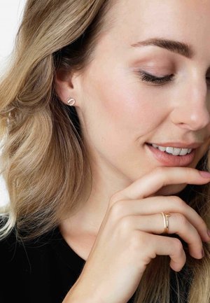 Boucles d'oreilles en or avec un design torsadé, présentant une surface lisse et un éclat subtil. Un gros plan d'une main touchant délicatement le visage.