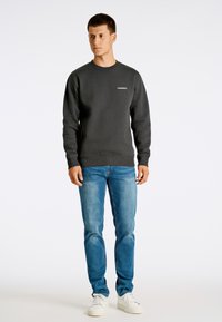 Sudadera gris oscura con cuello redondo, puños acanalados y logotipo blanco. Combinada con jeans de mezclilla azul claro y zapatillas blancas.