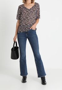 Hedvábná blůza s květinovým potiskem a krátkým rukávem v tmavých barvách, doplněná o rozšiřující se modré džíny. Texturovaná černá kabelka a černé kotníkové boty vzhled dotvářejí.