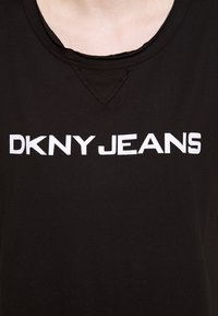 T-shirt noir avec un col rond et une petite découpe triangulaire. Présente un texte blanc audacieux indiquant "DKNY JEANS" sur la poitrine.