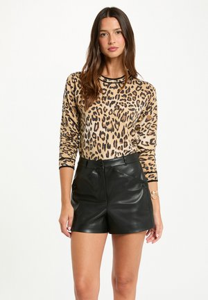 Maglione beige con stampa leopardata e dettagli neri abbinato a pantaloni corti in pelle nera a vita alta, con tasche frontali e texture liscia.