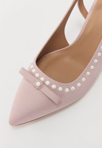 Chaussure à talon aiguille en daim rose avec un bout pointu, un nœud décoratif et des accents en perles le long du bord de l'ouverture. Texture lisse.