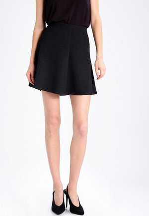 Jupe évasée noire en tissu texturé avec taille haute. Forme évasée, longueur genou, accompagnée de talons hauts noirs. Design simple et minimal.