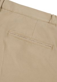 Beiger Stoff mit einer glatten Textur, der eine einzelne horizontale Rücken-Tasche mit genähten Akzenten aufweist. Einfaches und sauberes Design.