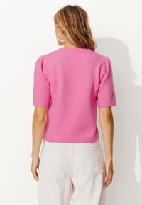 Un court pull en tricot rose avec un col rond et des manches courtes bouffantes, fabriqué en tissu doux, associé à un pantacourt en velours côtelé de couleur claire.