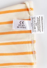 Baumwollstoff in Creme mit orangefarbenen Streifen, mit einem genähten Saum und Pflegeetikett, das UPF 40+, CE-Kennzeichnung und Waschanweisungen anzeigt.