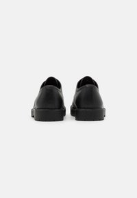 Black leather shoes with smooth texture, rounded shape, low profile, and solid rubber soles, viewed from the rear, showcasing stitching details.