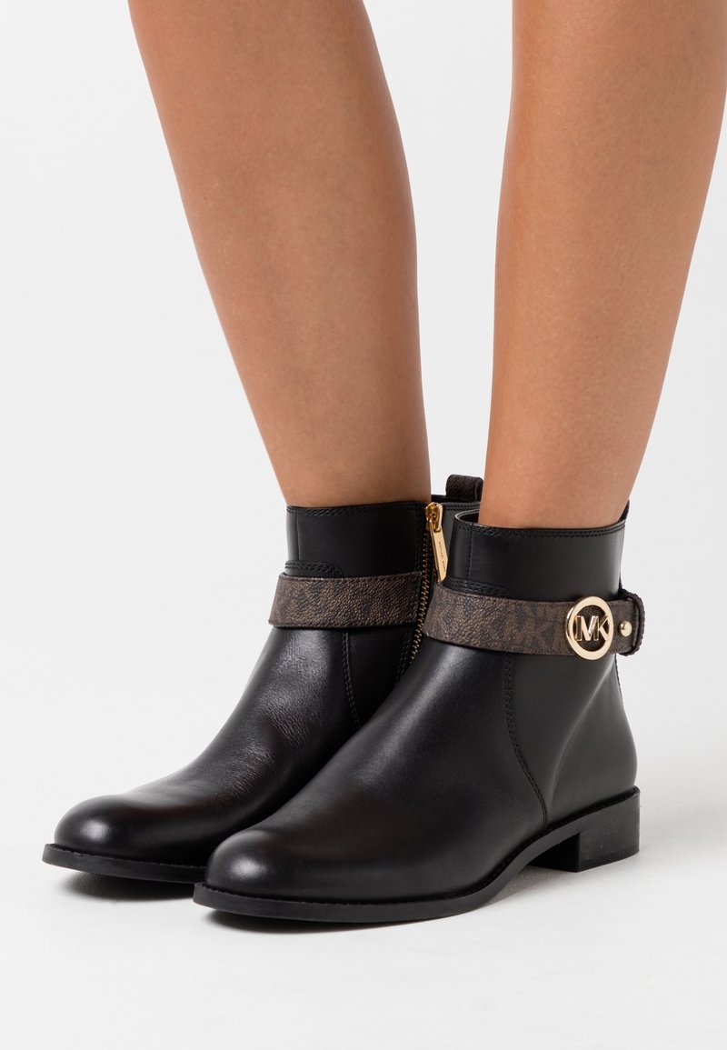 Bottines en cuir noir avec une sangle imprimée marron et des détails en métal doré, dotées d'une fermeture éclair sur le côté et d'un petit talon carré.