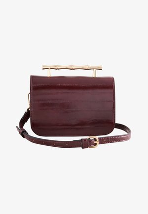 Donker bordeauxrode leren handtas met een gouden bamboe-stijl bovenhandgreep en een verstelbare band met een gouden gesp.