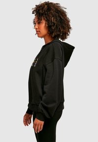 Black zip-up hoodie with a front pocket, ribbed cuffs, and hem. Features a colorful graphic design on the chest. Soft fabric texture.