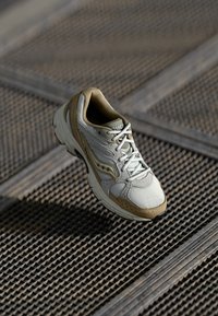 Sneaker i lys grå og beige, med mesh- og semsket skinnmaterialer, rund tå, snøringdesign og en teksturert gummisåle.