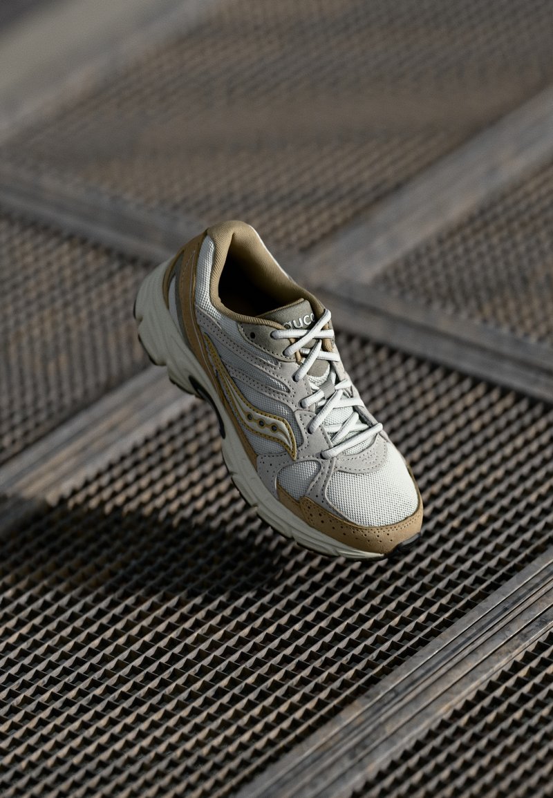 Sneaker i lys grå og beige, med mesh- og semsket skinnmaterialer, rund tå, snøringdesign og en teksturert gummisåle.