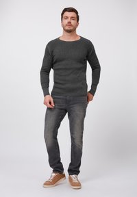 Grau gerippter Pullover mit weitem Ausschnitt und langen Ärmeln, kombiniert mit dunkelgrauen Jeans und sandfarbenen Sneakers. Glatte Stoffstruktur.