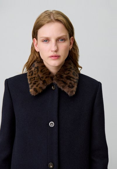 Abrigo de lana en color azul marino con un cuello de piel sintética de leopardo, que presenta un cierre de botones y una silueta estructurada. Textura suave y diseño clásico.