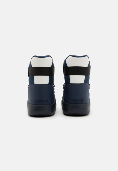 Korkeat tennarit, jotka ovat tummansiniset ja valkoiset, tekstuuripinnalla, kaksilla hihnoilla ja pyöreällä varvastyönnöllä. "MOON BOOT" on kohotettu kantapäällä.