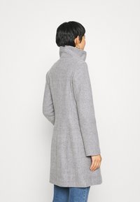 Grijs wollen jas met een hoge kraag, getailleerde pasvorm en naadloos ontwerp. De achterzijde toont schone lijnen en een textiel met structuur.