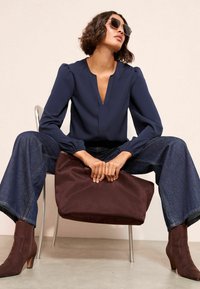 Jūras spēku zila blūze ar V veida kakla izgriezumu un puffed pleciem, pārī ar platām kājām denim biksēm, brūniem zamšādas potīšu zābakiem un brūnu somu. Gluda tekstūra.