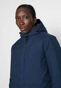 Navy blue insulated jacket with a zip closure and adjustable hood. Smooth texture with a fitted design, featuring no visible patterns or accents.