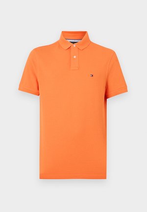 Polo orange en coton, avec un col classique, une patte à deux boutons et un petit logo sur la poitrine gauche. Manches courtes.