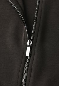 Černá zipová bunda s hladkým povrchem, vybavená kovovým zipem a čistým, minimalistickým designem. Tahátko zipu je v stříbrné barvě.