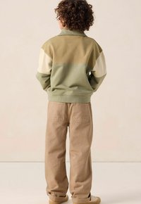 Groen en beige kleurgebloqueerde sweatshirt met een kraag, gecombineerd met tan, losse broeken met twee achterzakken. Getextureerde stof.