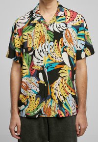 Chemise à manches courtes avec un imprimé coloré de banane et de toucan sur fond noir, en tissu léger avec fermeture à boutons.
