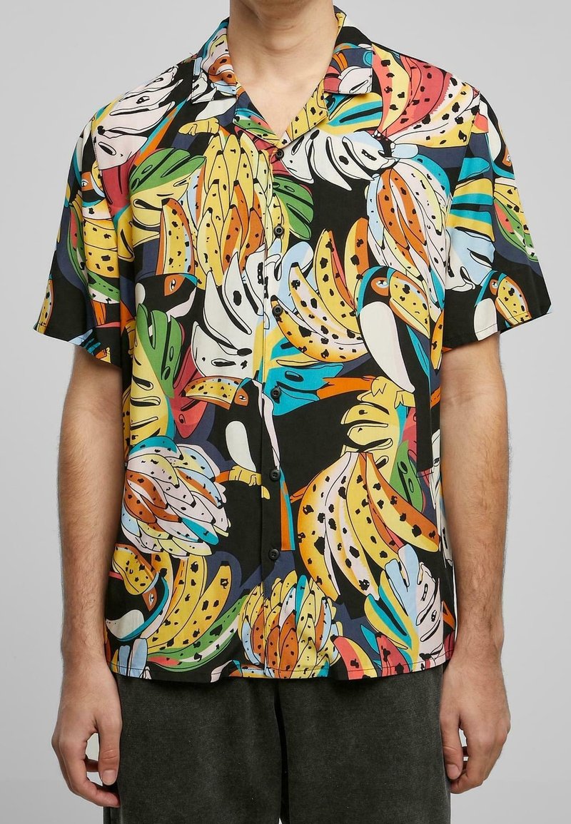 Chemise à manches courtes avec un imprimé coloré de banane et de toucan sur fond noir, en tissu léger avec fermeture à boutons.