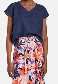 Haut en lin bleu marine avec un col en V et des manches courtes, accompagné d'une jupe fleurie arborant des motifs tropicaux orange, rose et bleu.