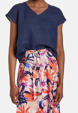 Laivastonsininen pellavapaita, jossa on V-aukko ja lyhyet hihat, yhdistettynä kukkakuosiseen hameeseen, jossa on oransseja, vaaleanpunaisia ja sinisiä trooppisia kuvioita.