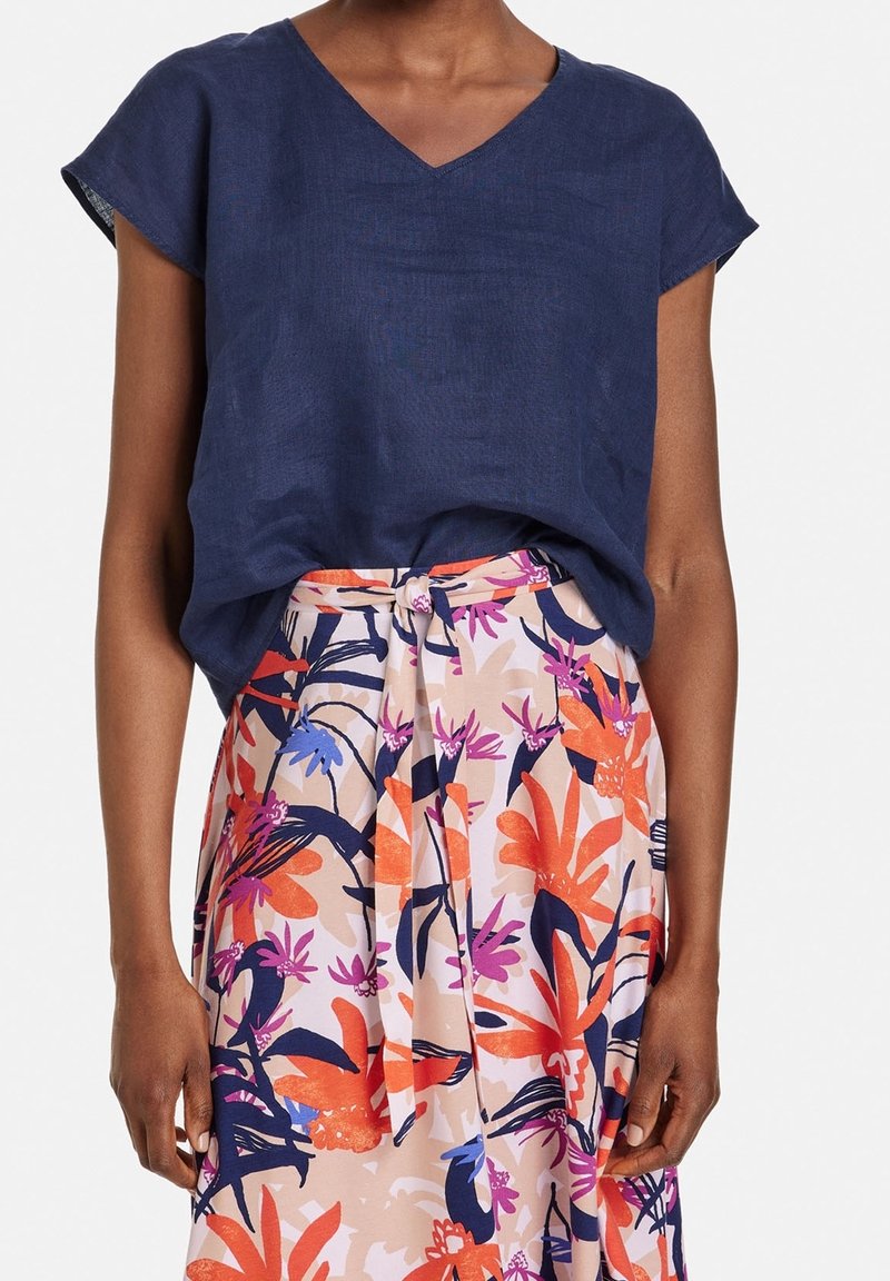 Haut en lin bleu marine avec un col en V et des manches courtes, accompagné d'une jupe fleurie arborant des motifs tropicaux orange, rose et bleu.