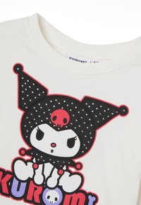 Weißes T-Shirt mit einer Cartoonfigur, die einen schwarzen Punktmützenhut trägt, roten Akzenten und dem Text "KUROMI" in leuchtenden Farben.