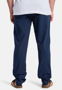 Pantalones de algodón azul marino con un corte relajado, costuras visibles y dobladillos enrollados, combinados con sandalias marrones en pies descalzos.