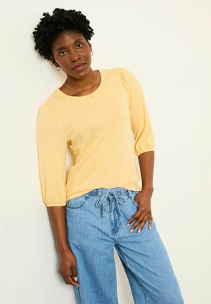 Light yellow, long-sleeve top with puffed shoulders, paired with loose blue denim pants featuring a drawstring waist.