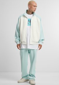 Helleblau und weiße Zip-Jacke mit Stehkragen, kombiniert mit passender Hose und einem weißen Grafik-T-Shirt. Glatte Textur, sportliches Design.