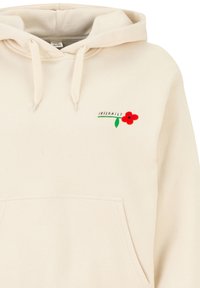 Cremfarbener Kapuzenpullover aus weichem Stoff, mit einer Fronttasche und roter Blumenstickerei mit grünem Stängel auf der linken Brustseite.