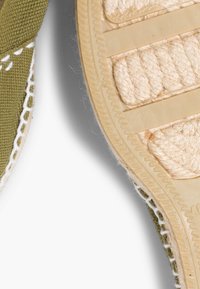 Baskets en toile verte avec des coutures blanches, présentant une semelle intermédiaire en jute beige texturé et une semelle extérieure en caoutchouc, mettant en valeur un motif naturel en tissage.