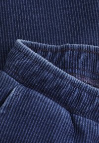 Zbliżenie niebieskiego materiału prążkowanego, ukazujące szczegółową strukturę i wszyty szew.