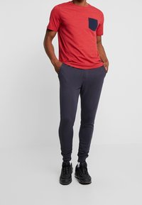 Röd prickig t-shirt med en marinblå ficka, tillsammans med mörkgrå sweatpants. Slim fit, material i bomullsblandning och elastiska ärmar vid anklarna.