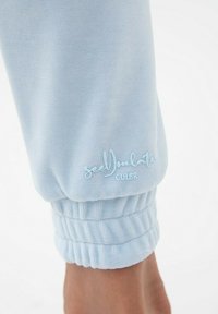 Jasnoniebieskie dżinsowe joggery z elastycznym paskiem w talii, z marszczonymi mankietami i haftowanym logo w kontrastowym kolorze.