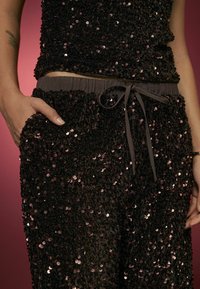 Top negro con lentejuelas combinado con pantalones a juego, que cuentan con una cintura elástica con cordón y una superficie texturizada y brillante.