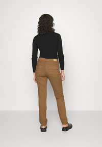 Calças de algodão castanho com um design ajustado, apresentando bolsos traseiros, detalhes de costura e um rótulo visível na cintura.