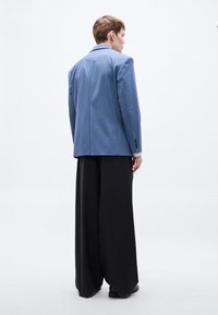 Sacou albastru cu dungi fine și design structurat, asortat cu pantaloni largi negri, creând un contrast de forme și culori.