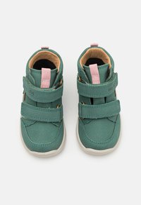 Zapatillas altas de imitación cuero verde con dos correas de Velcro rosas, suelas blancas y un interior suave. Presenta costuras decorativas.