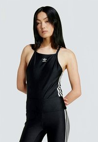 Fekete sportos atlétatrikó fehér Adidas logóval, spagettipántokkal és fehér oldalsávokkal, fekete, testhezálló leggingszel párosítva.