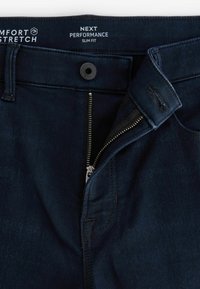 Vaqueros ajustados azul oscuro hechos de una tela elástica cómoda, que presentan un cierre de cremallera metálica, botón de cierre y diseño de cinco bolsillos.